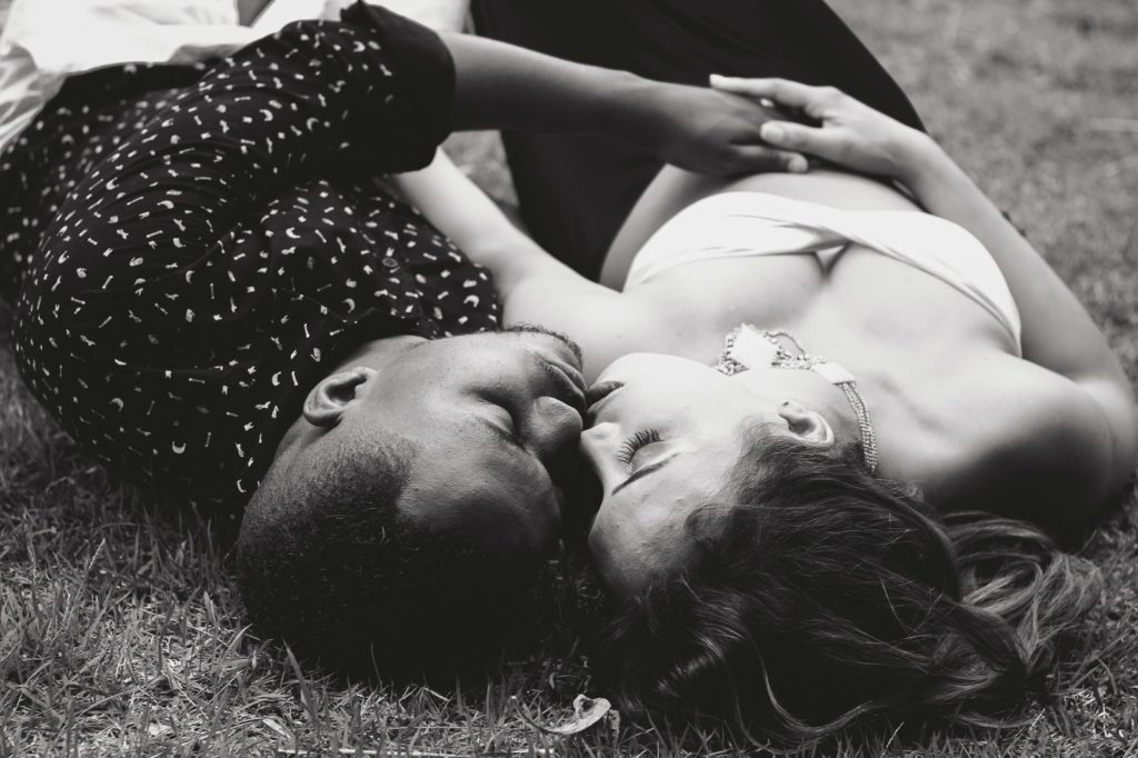 grayscale photo of man and woman facing each other and lying on grass