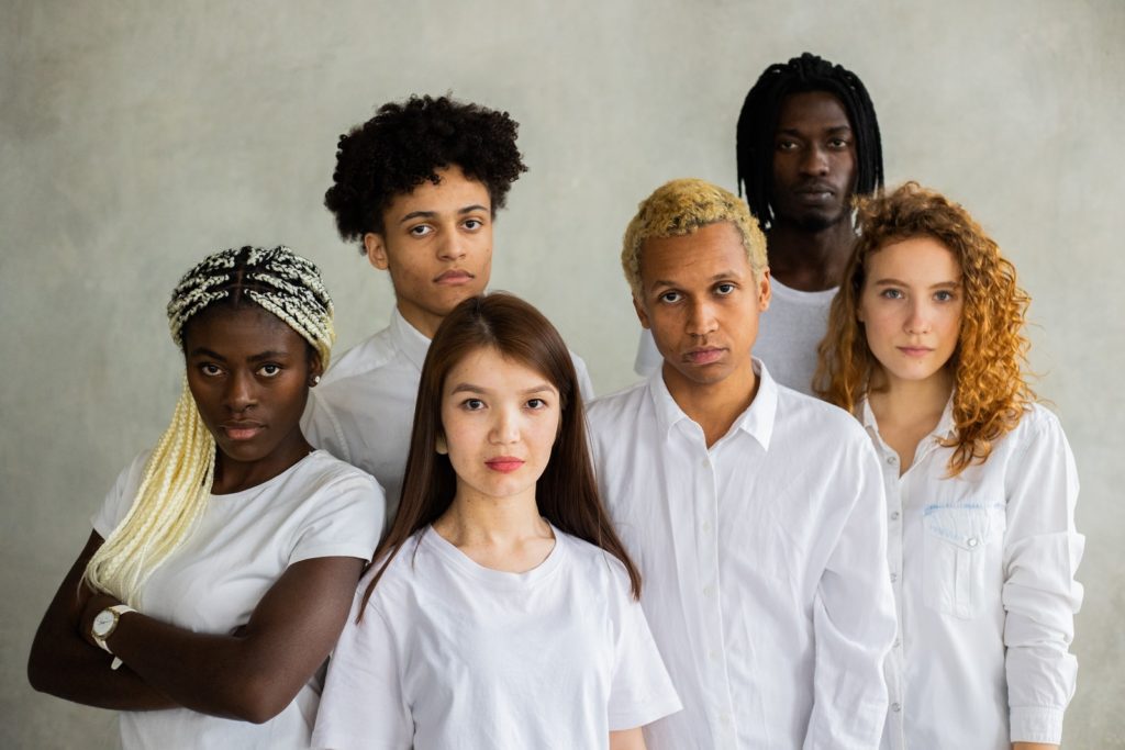 Serious diverse multiracial people standing close together representing concept of unity and looking at camera against gray background